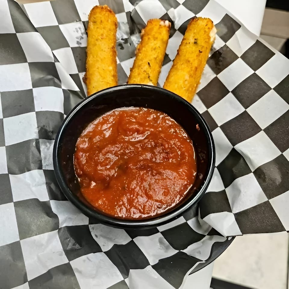Three golden-brown mozzarella sticks and a black bowl of marinara sauce on checkered paper.