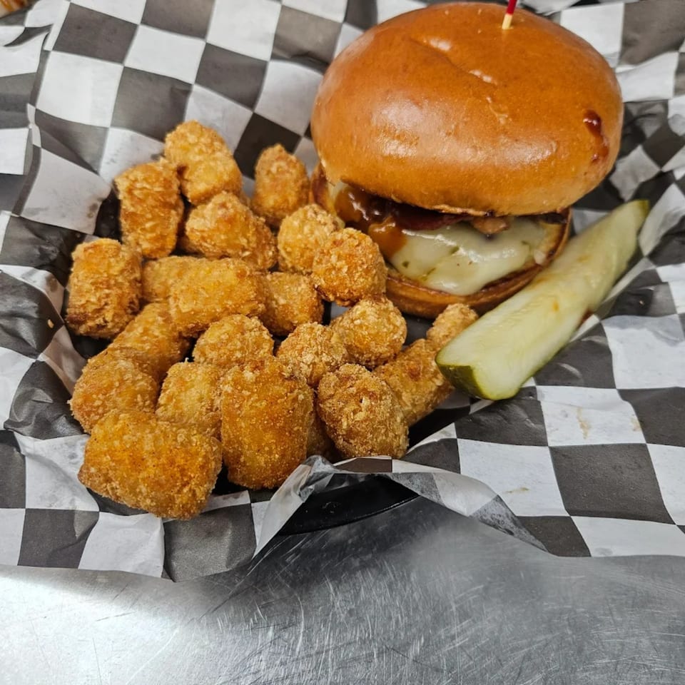 A burger with melted cheese and caramelized onions, tater tots, and a pickle spear.